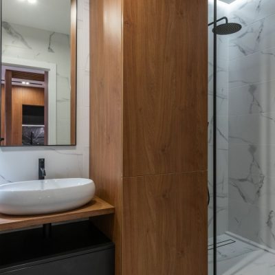 Home Interior of contemporary bathroom with wooden cupboard placed between sink and shower cabin