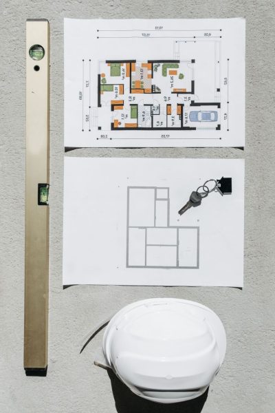 Blueprints, spirit level, and hard hat symbolize house planning.